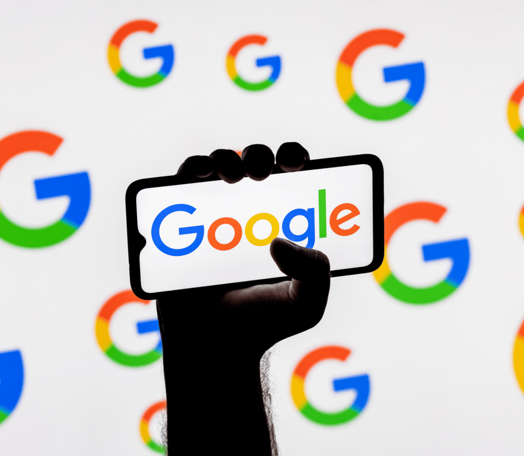 Hand holding smartphone displaying the name Google on a background of Google Gs