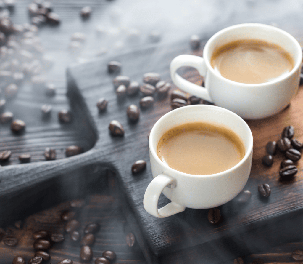 Two cups of fresh coffee, surrounded by coffee beans on a dark background