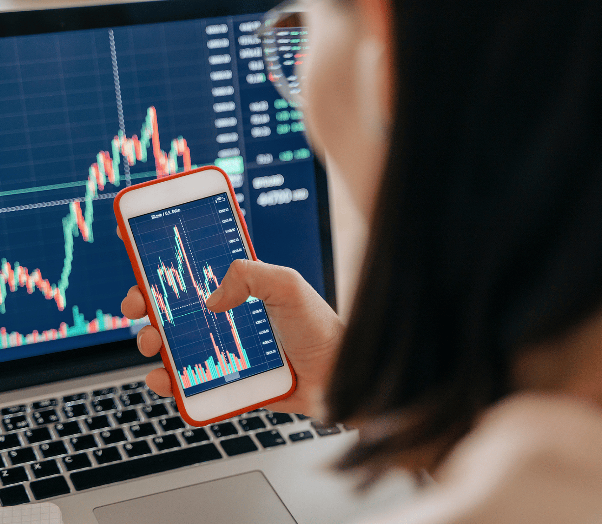 Woman uses smartphone and computer to analyze the stock market and her stocks.