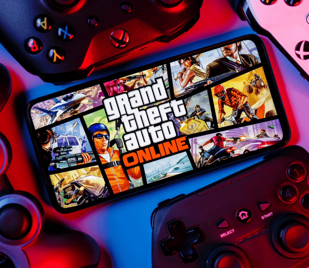 Grand Theft Auto Online on a smartphone, surrounded by PS5 and Xbox controllers