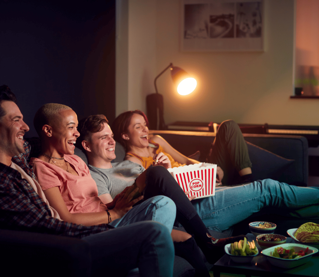 Group of friends eating popcorn on couch while watching a movie at home