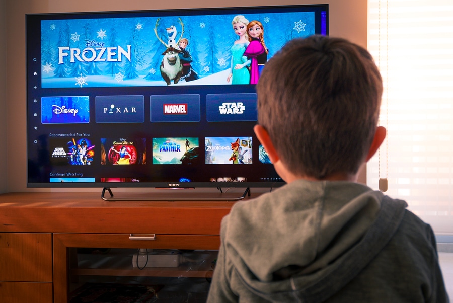 Back view image of cute little boy watching the new Disney plus platform on TV