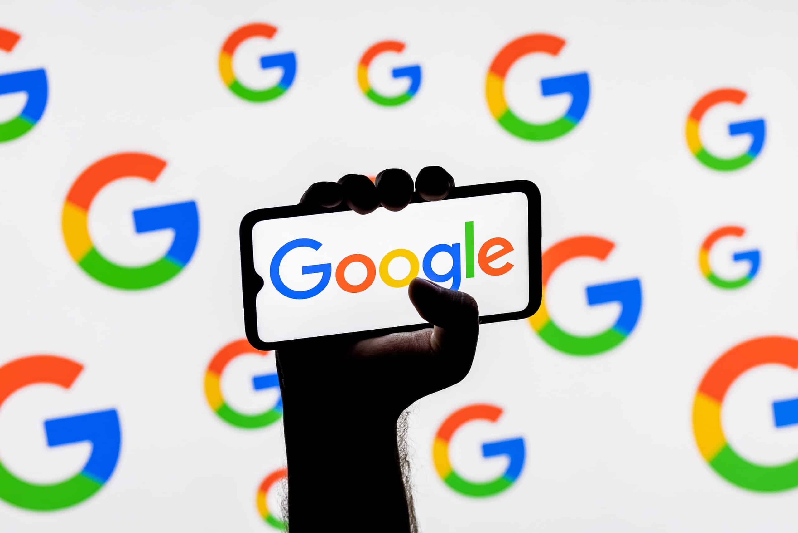 Smartphone with the Google technology company logo on the screen in a clenched hand on the background of Google logos