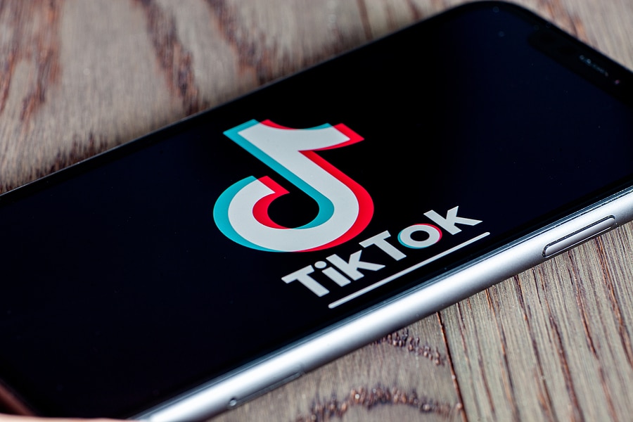 TikTok application icon on Apple iPhone 11 screen close-up. Hand holding smartphone Tik Tok icon on wooden background.  Tiktok Social media network