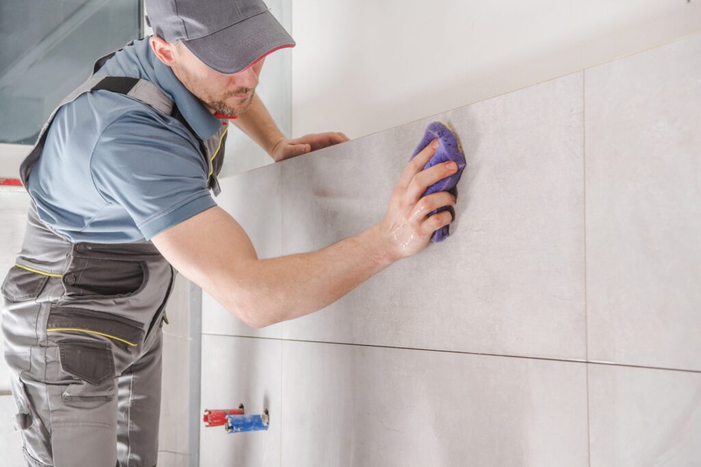 Home Improvement Theme. Caucasian Contractor Worker in His 30s Finishing Ceramic Tiles in the Bathroom.