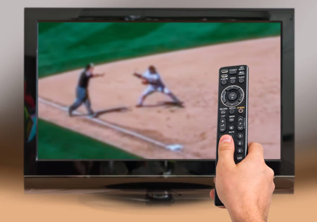 Man is watching baseball match on TV and holds remote controller in hand