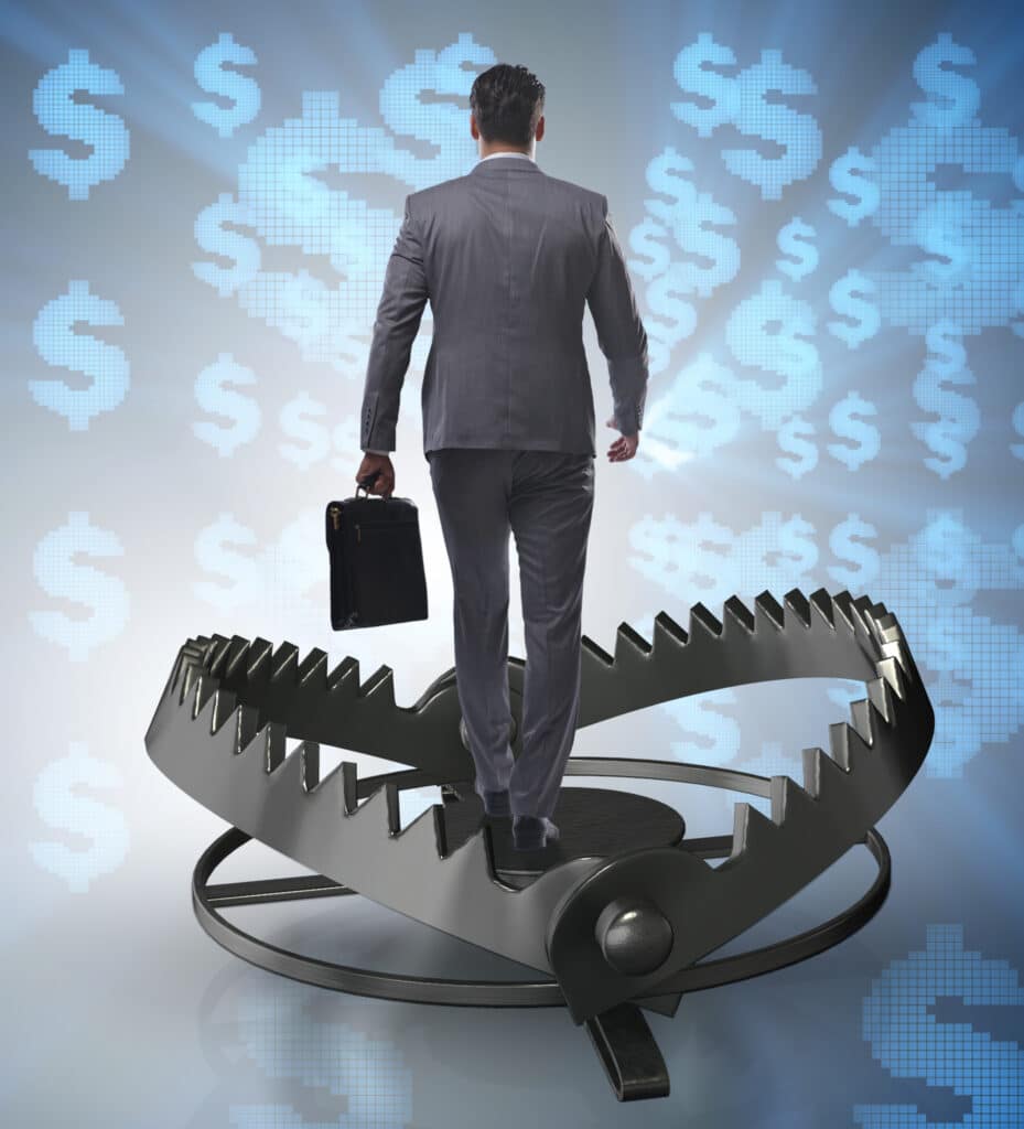 Businessman standing in the center of a steel trap with blue dollar signs on a black background