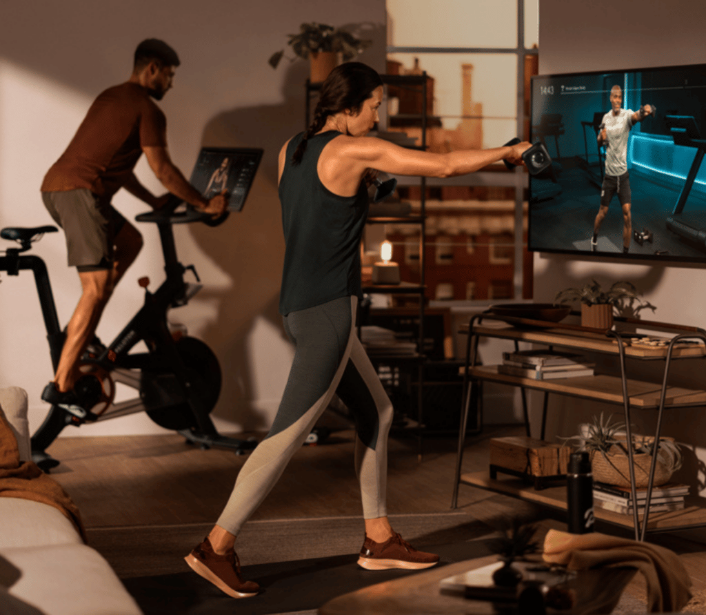 Man on Peloton bike, woman doing Peloton workout on screen