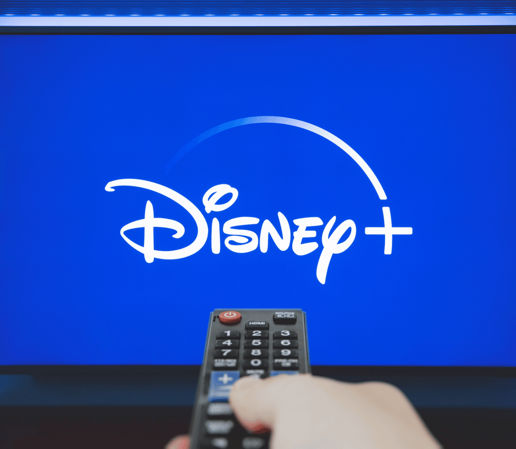 Viewer pointing remote at TV displaying Disney+ logo on blue backgroundeen