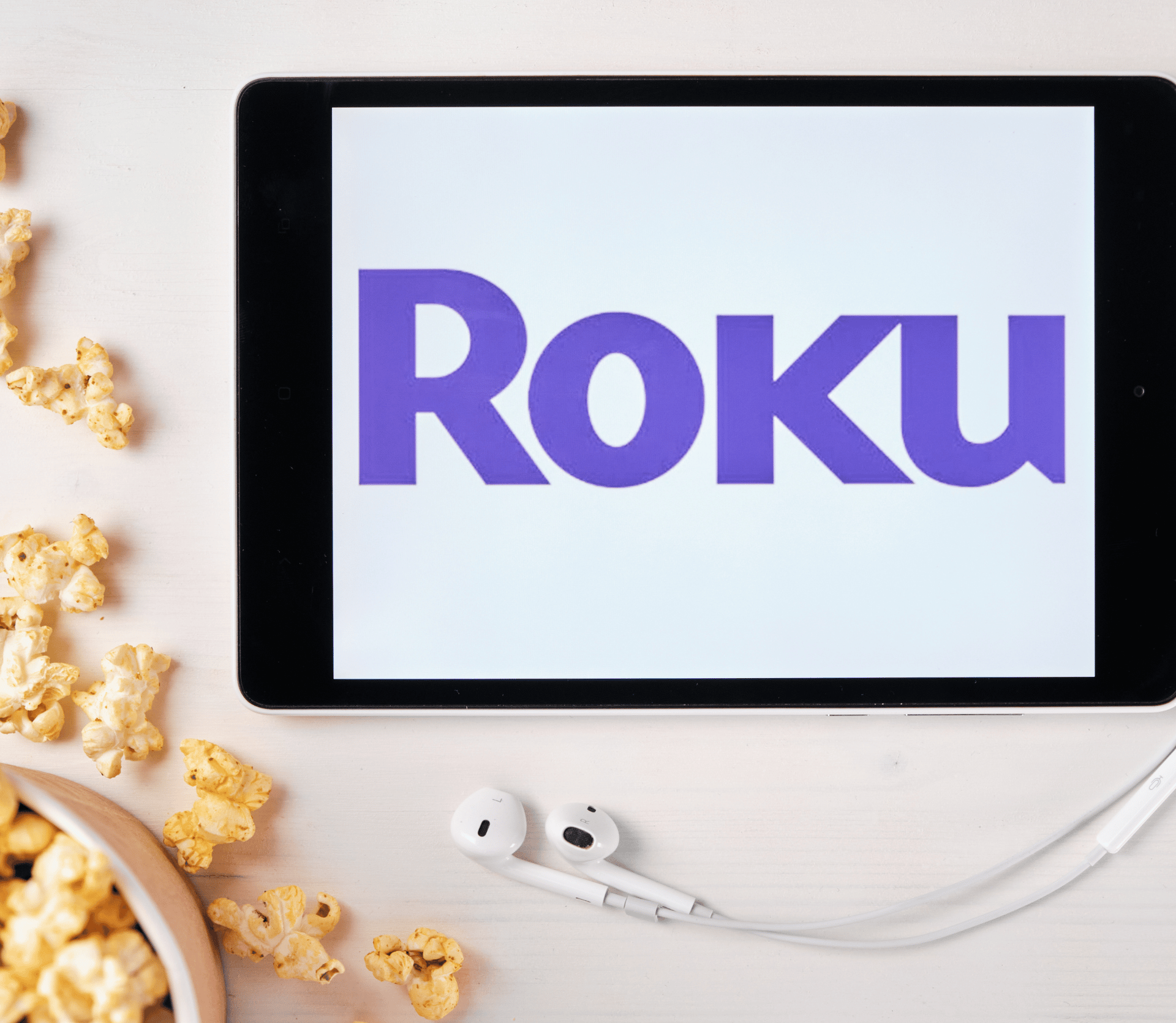 Roku logo displayed on tablet, next to spilled popcorn and earbuds