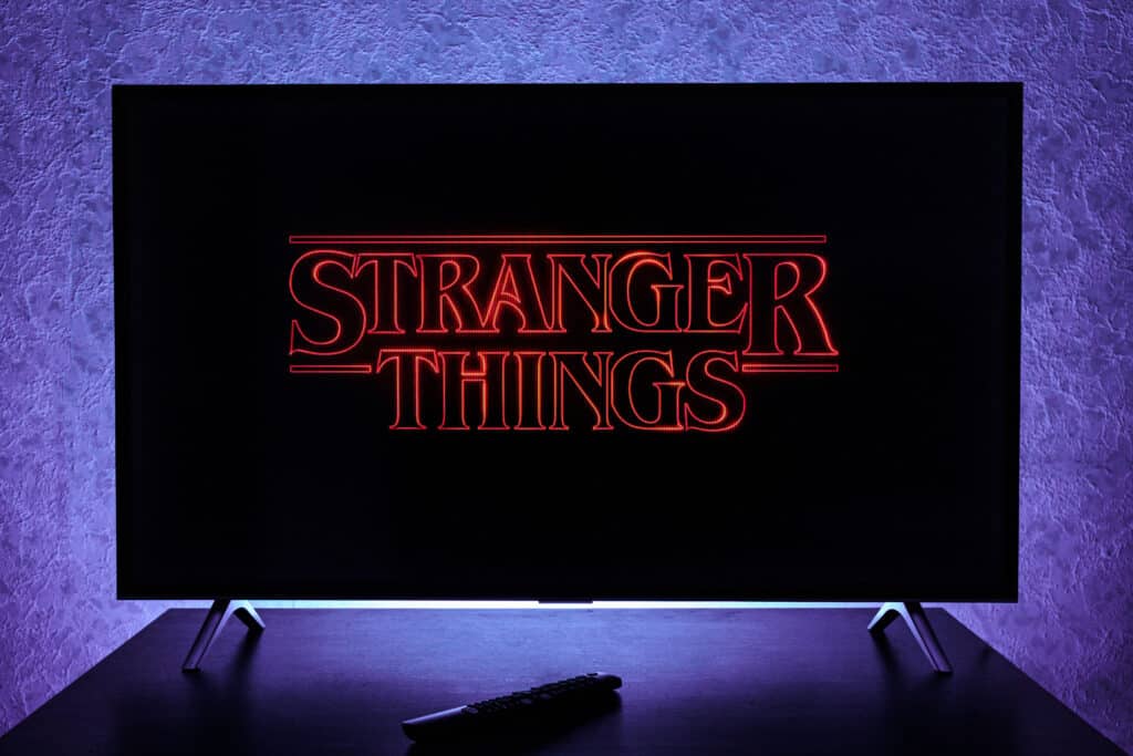 Stranger Things logo on big screen TV backlit with a purple glow.