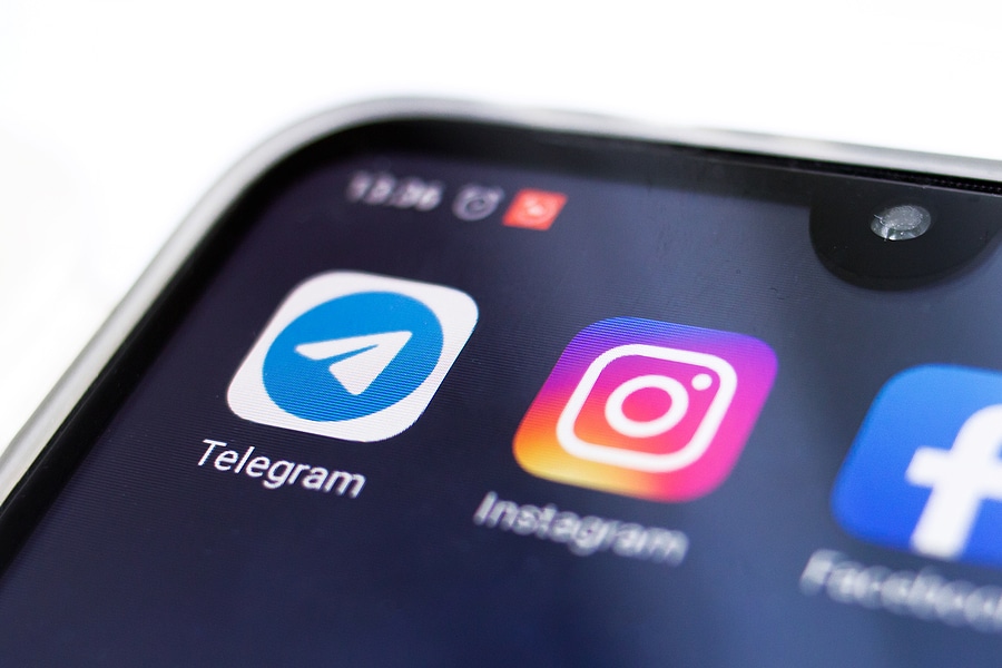 Telegram icon on smartphone, next to Instagram and Facebook icons.