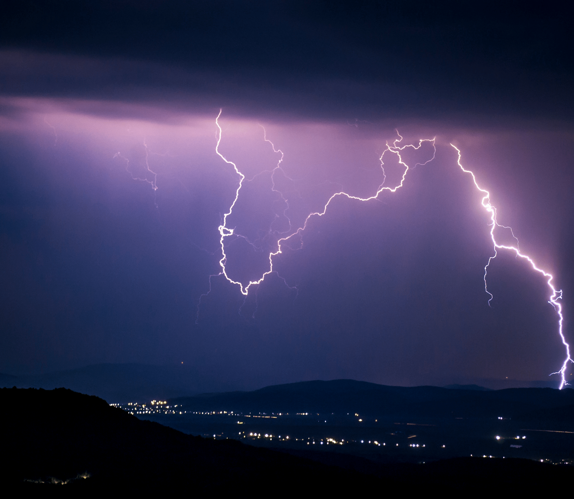 Lightning in the night sky over a city in the distance