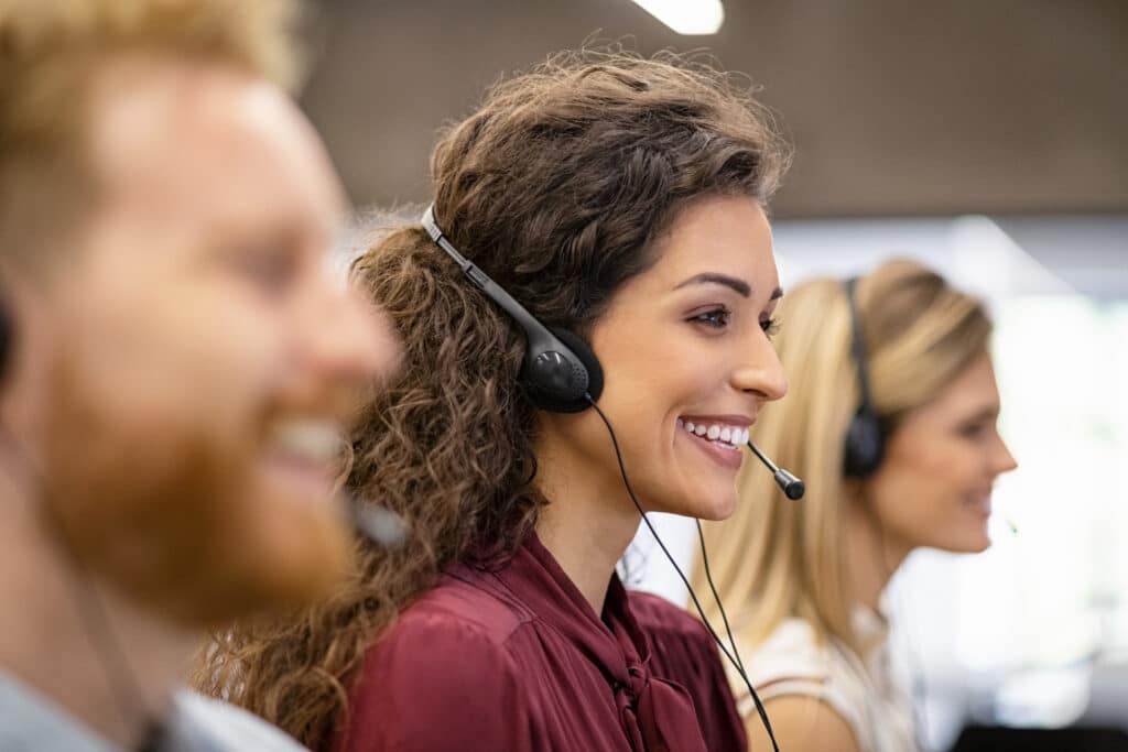 Call center team making calls to customers. Center woman is the focus and she's smiling as she talks to her customer.