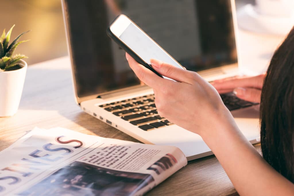 Cropped view of businesswoman working with smartphone, laptop and newspaper at workplace in office