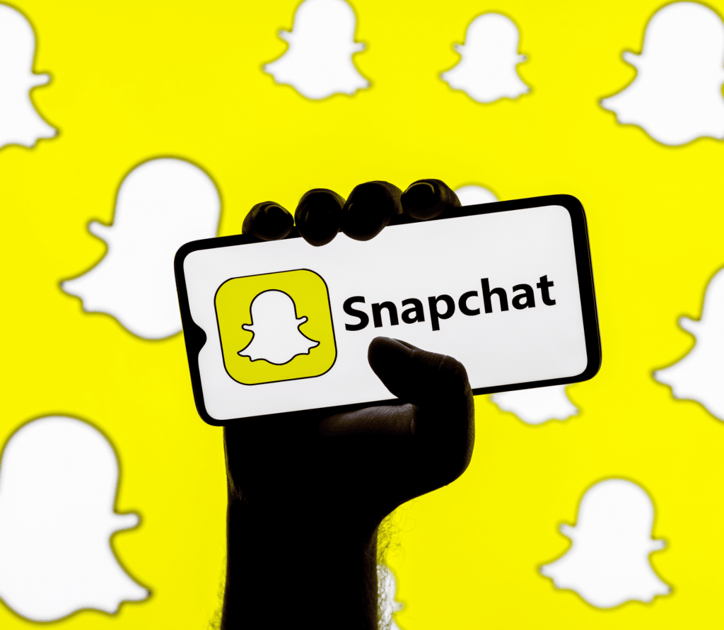 Hand holding a smartphone with Snapchat logo on yellow background with Snapchat logo