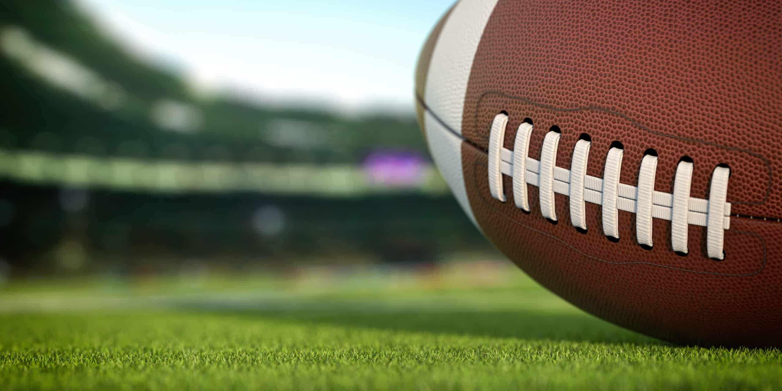 American football ball on grass of football arena, 3d illustration