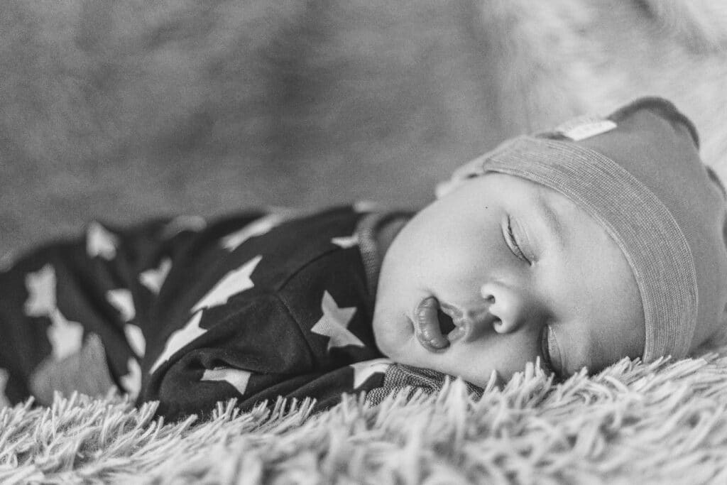 sleeping newborn baby on a blanket in hat open mouth black and white noise image