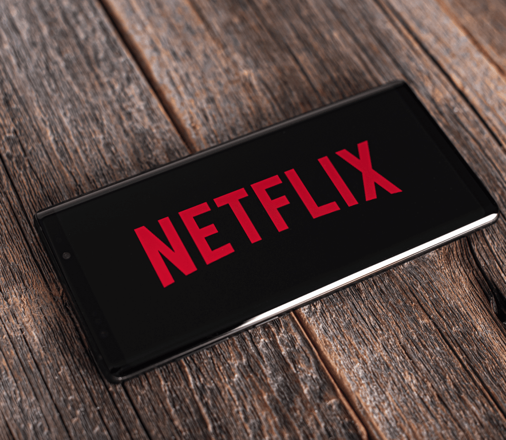 Netflix logo displayed on a smartphone that is sitting on top of a wooden tabletop