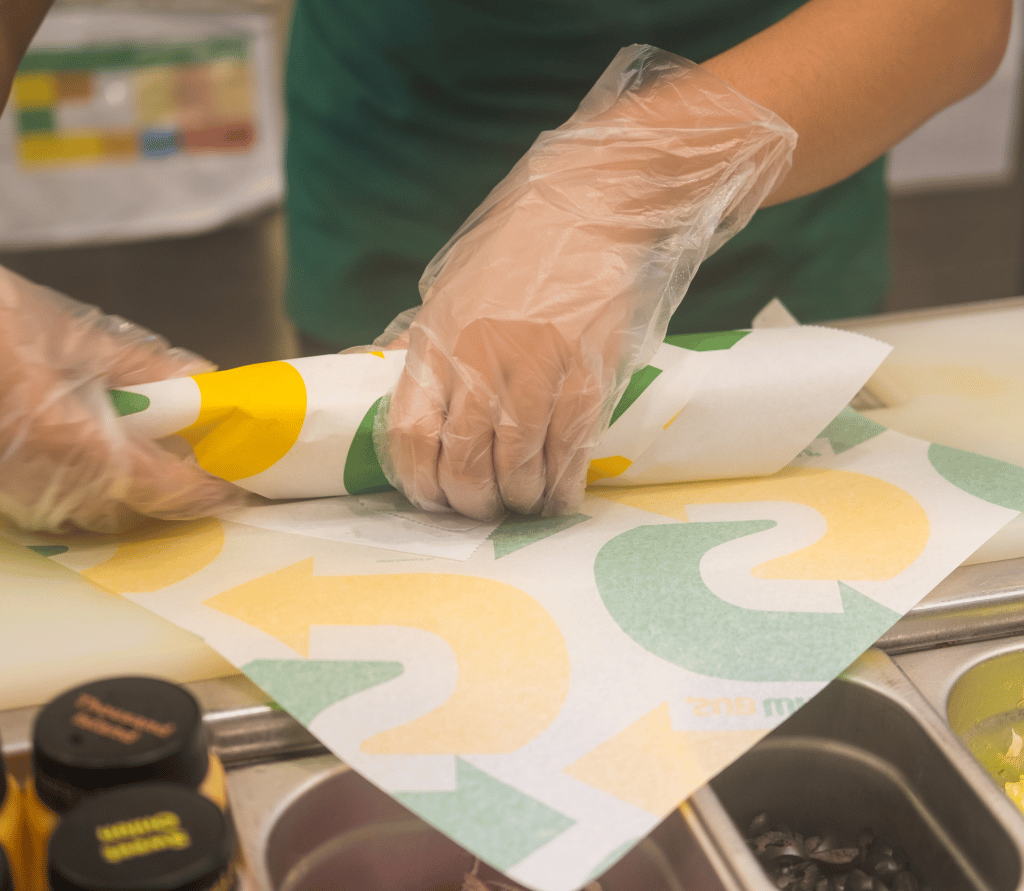 Subway restaurant employee rolls up sandwich in waxed paper with the Subway logo on it.