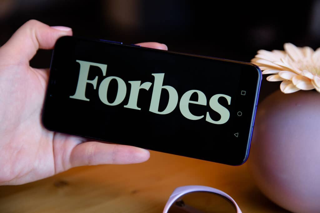 Person holding smartphone with Forbes logo displayed on black backgroun