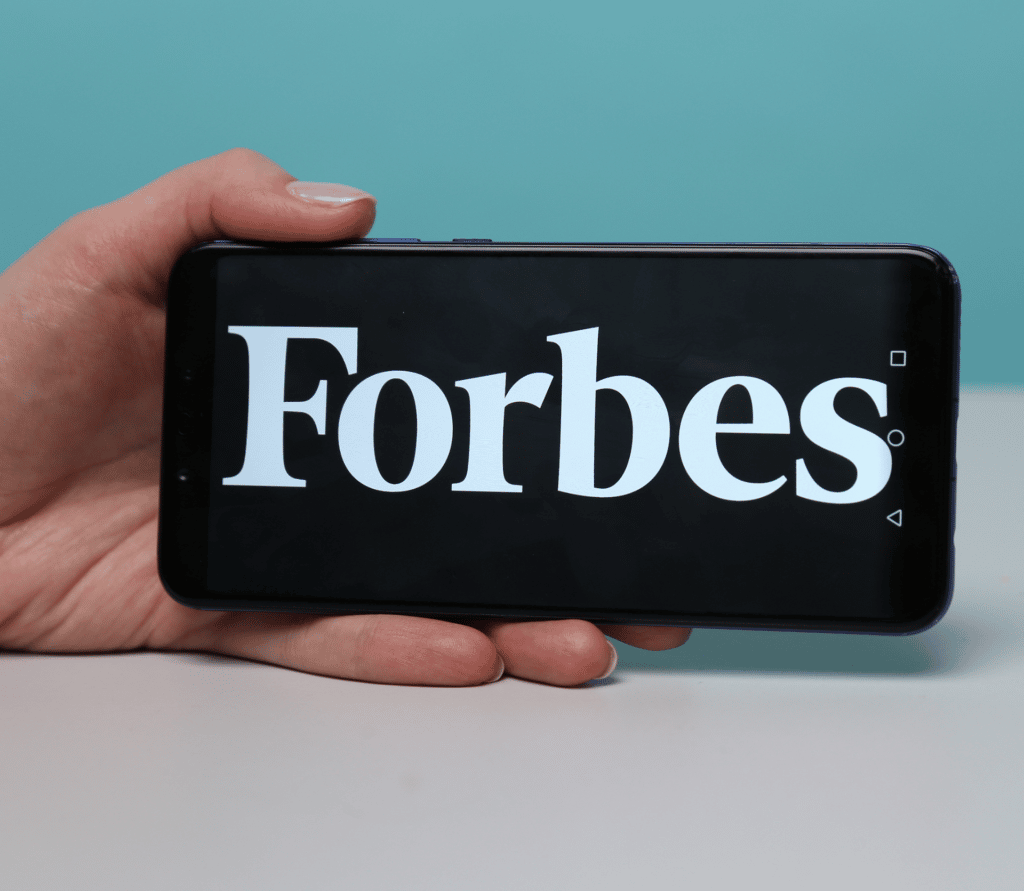 Person holding smartphone with Forbes logo displayed