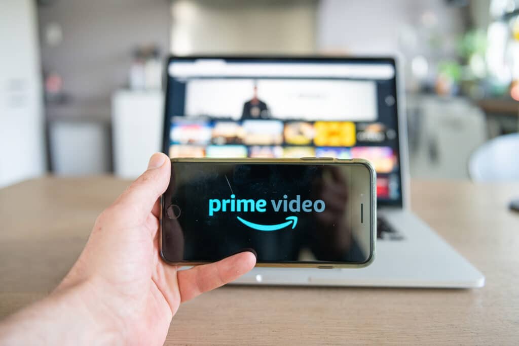 Prime video logo on mobile phone. Smartscreen on laptop, Amazon prime video online video, content streaming subscription service.