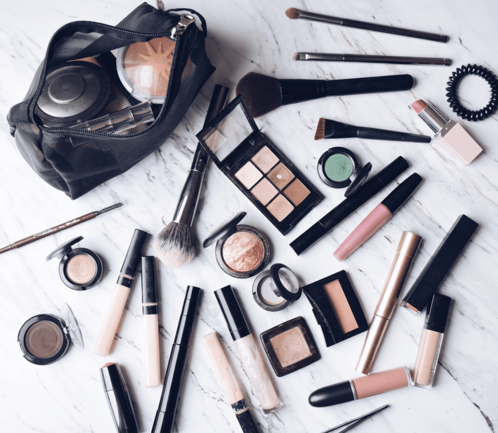 A variety of beauty products, brushes and a make-up bag spread out on a marble countertop