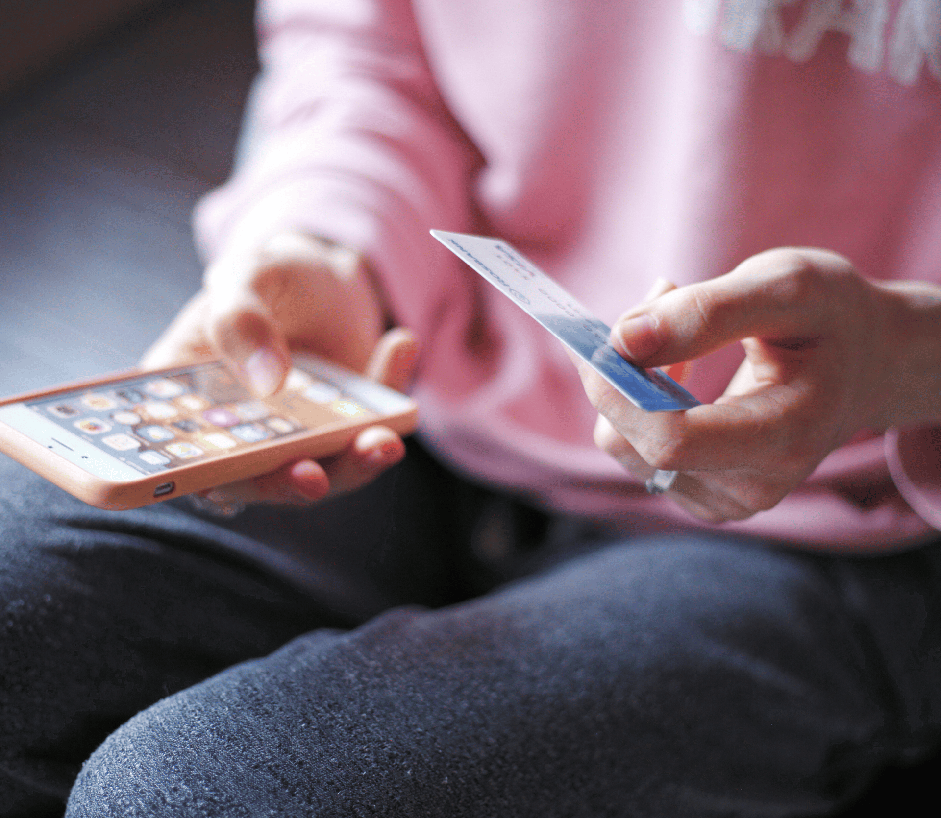 Shopper in pink sweatshirt and blue jeans makes an online purchase on their phone.