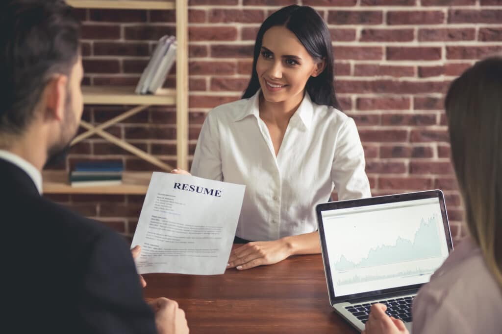 Female job candidate is being interviewed by two HR employees, while reviewing her resume