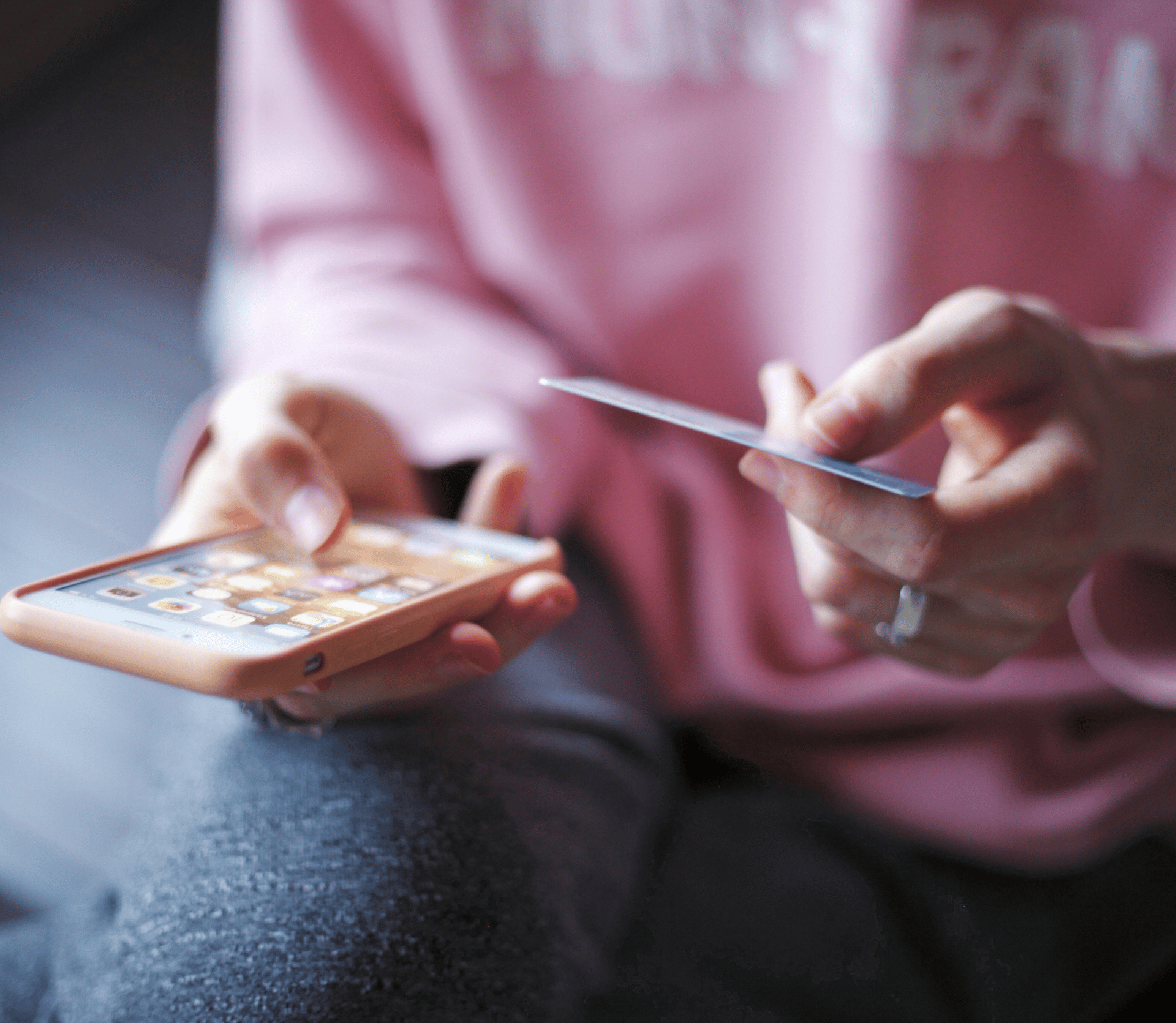 Woman in pink sweatshirt making an online purchase with a credit card on her iPhone