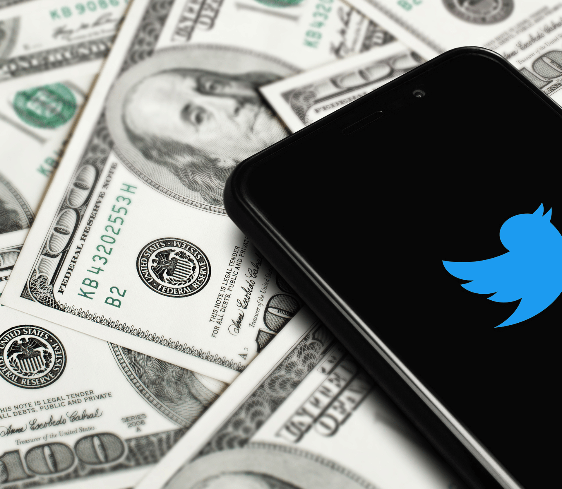 Twitter logo on black background on smartphone, lying on top of hundred dollar bills