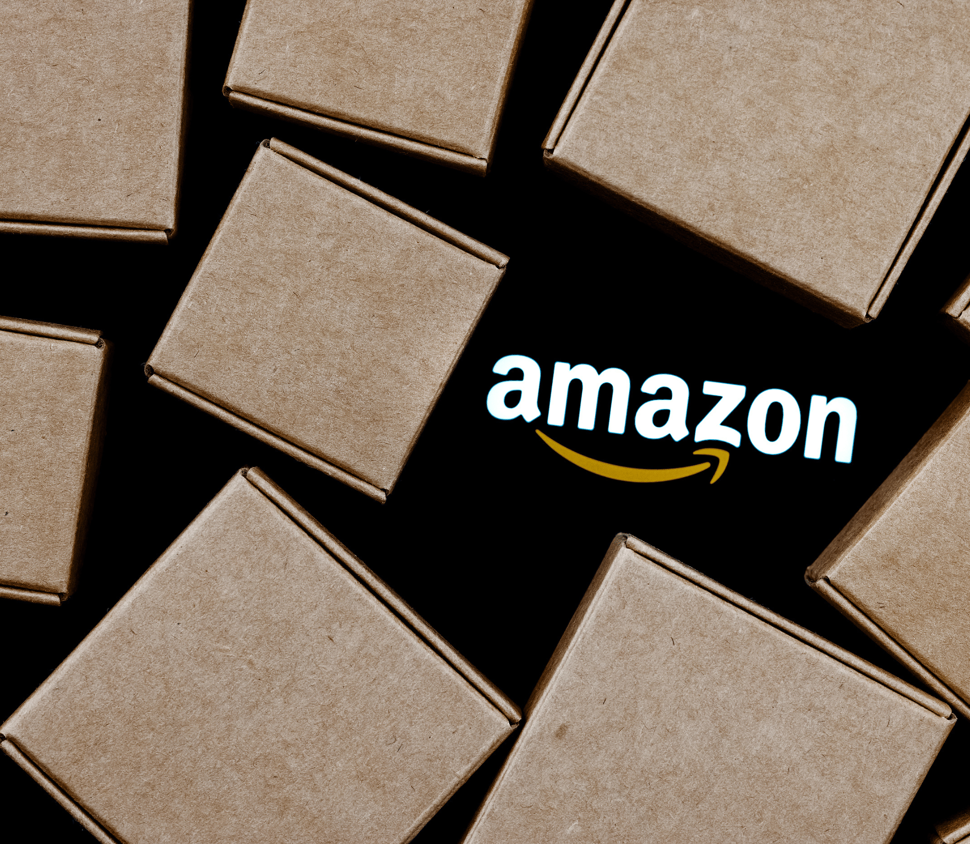 Amazon logo on black background, surrounded by cardboard boxes