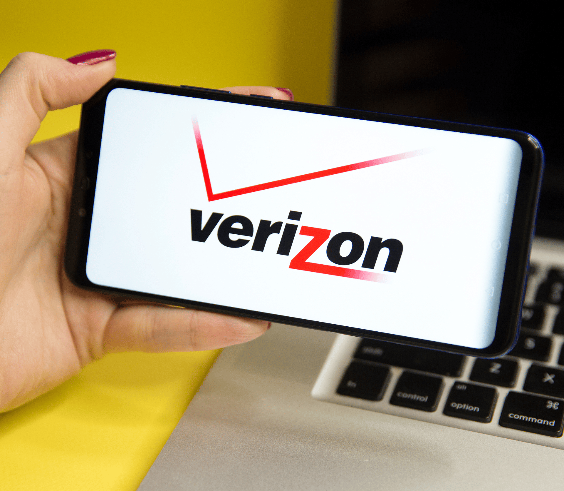 Woman holding cell phone with Verizon logo on it. Laptop in background.