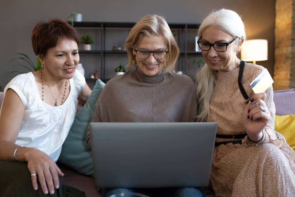 Happy senior women using computer together on the sofa, they doing shopping online and paying with credit card