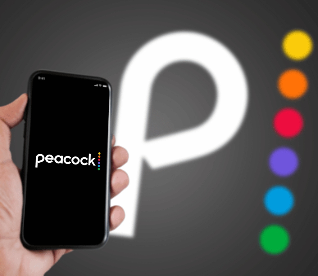 Hand holding a phone with the Peacock Tv mobile app on the screen and the Peacock Tv logo blurred on a grey background. Peacock is an American video streaming service