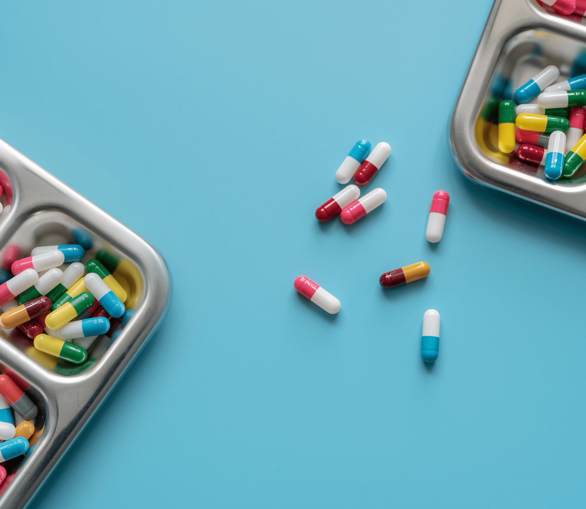 Multi-colored capsule pills in stainless steel tray and on blue background. Pharmacy banner. Pharmaceutical industry. Pharmaceutics. Prescription drugs. Medical and healthcare.