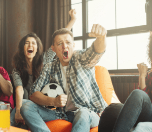 A group of young adults sitting on a couch cheering on their soccer team.