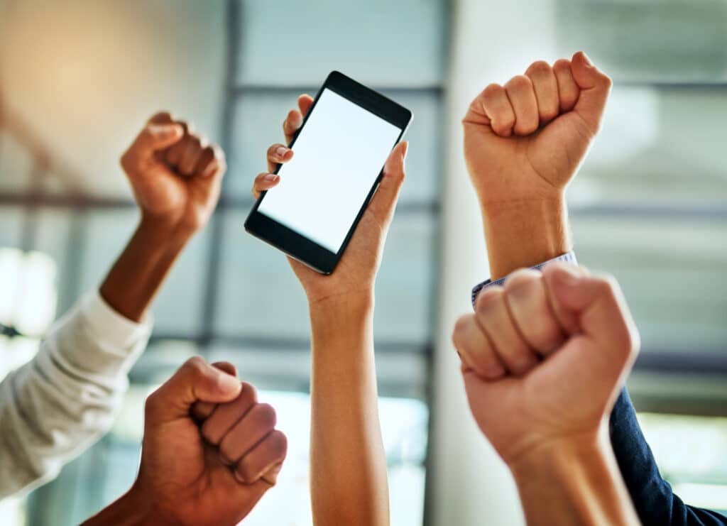 Four fists in the area with a fifth hand holding a smartphone with a blank screen, indicating sports fans watching a standalone sports app.