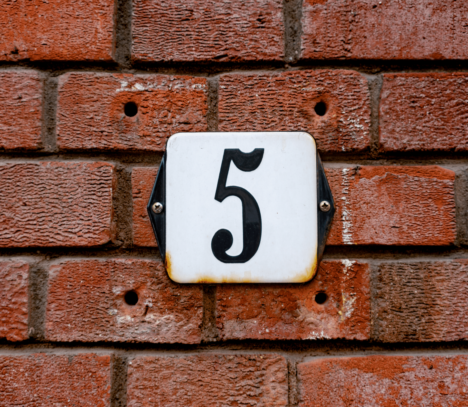 Black number 5 on a white tile, affixed to a red brick wall