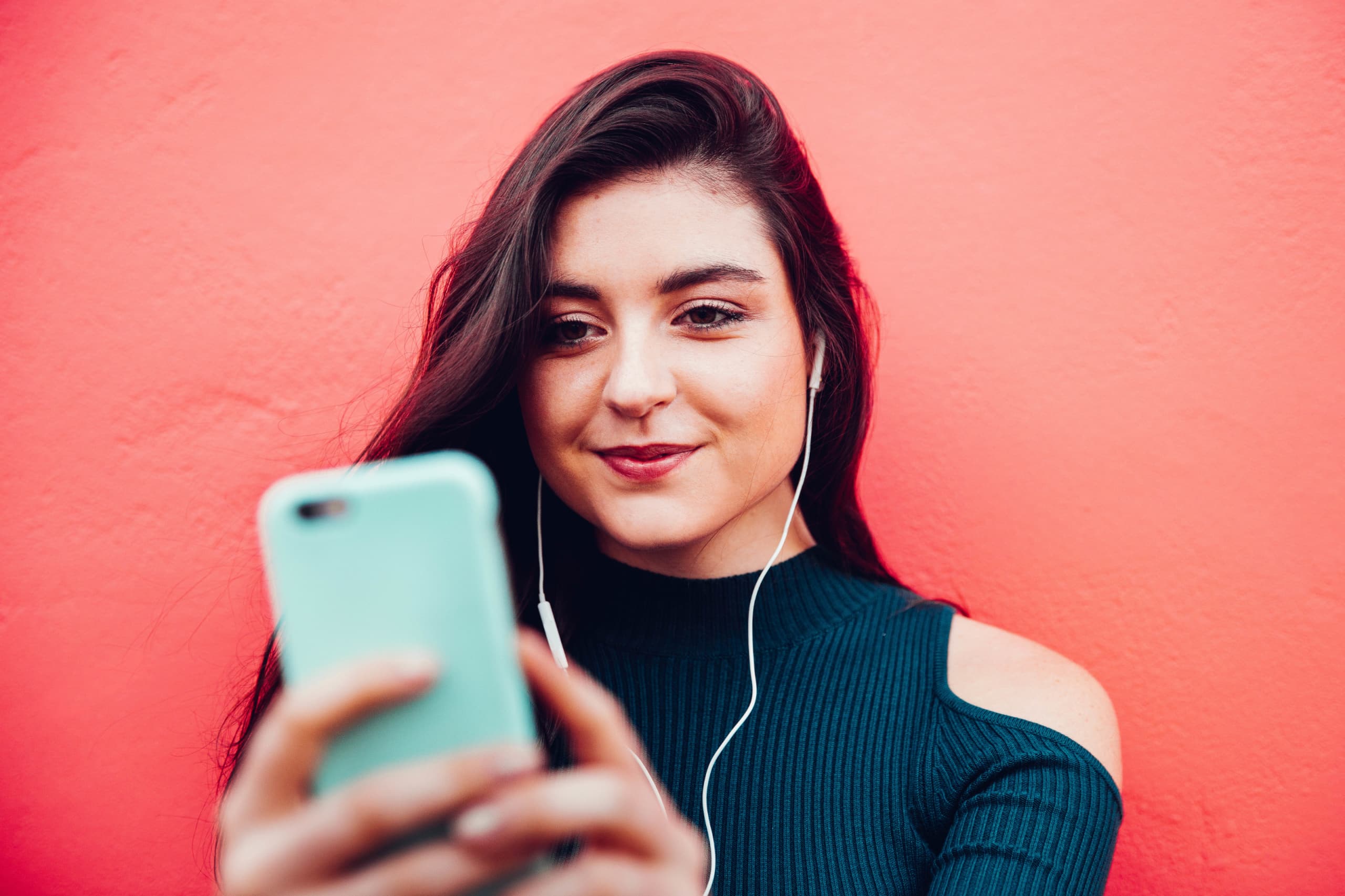 Woman holding smartphone, listening with headphones.