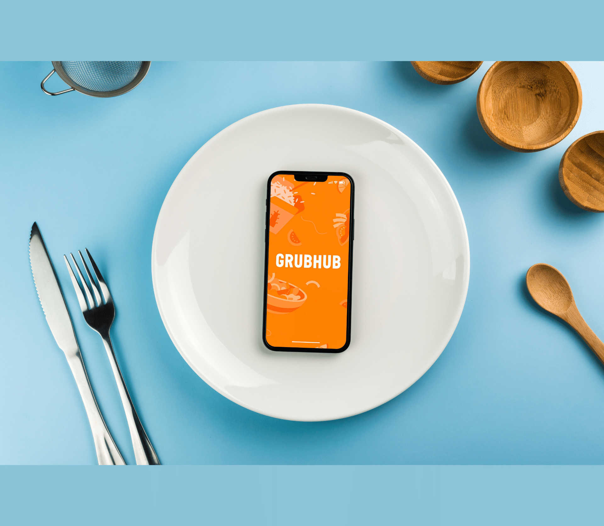 GrubHub app on a smartphone on top of a white dinner plate and blue tablecloth