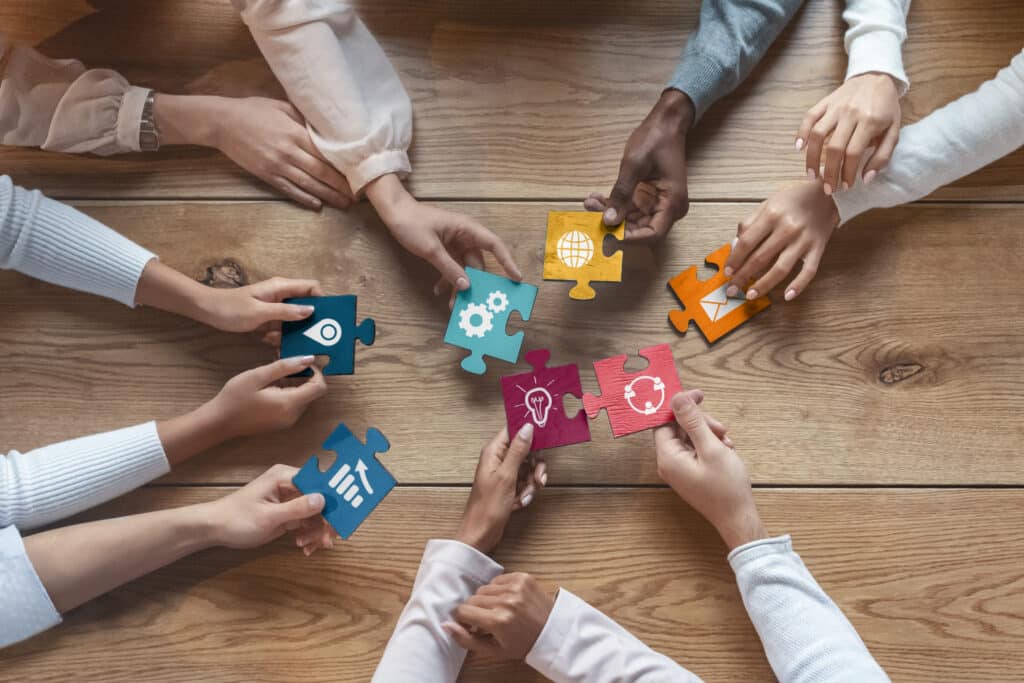 International team of coworkers sitting around table, putting colorful puzzles together, teamwork concept, top view, practicing a resource assessment exercise