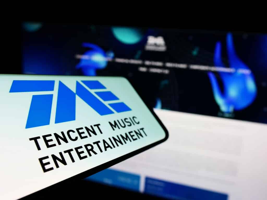 Smartphone with logo of Chinese company Tencent Music Entertainment Group on screen in front of business website. Focus on left of phone