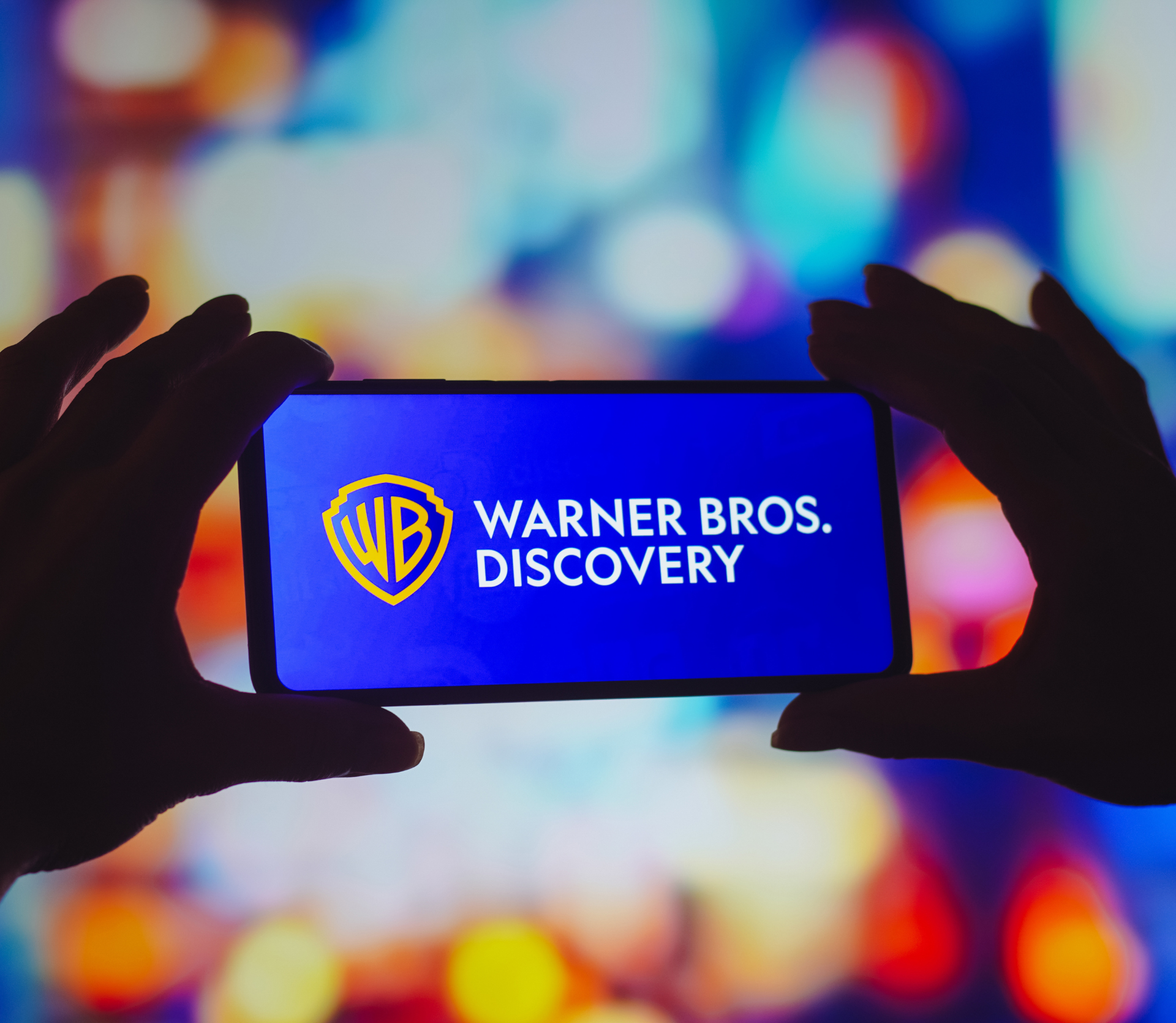 Warner Bros. Discovery logo on smartphone with colorful background behind it.