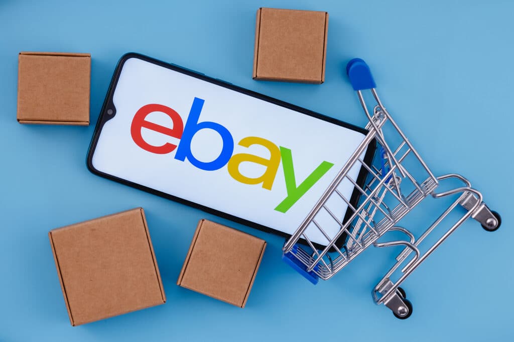 Smartphone with eBay logo on the screen, shopping cart and parcels.