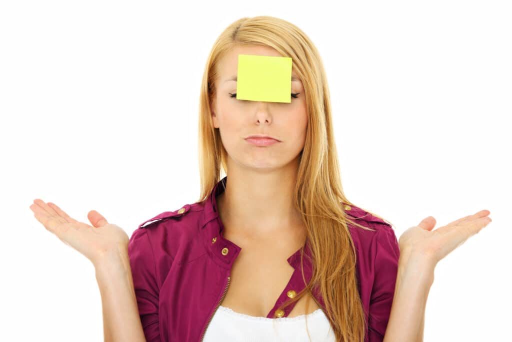 A photo of a young blonde woman with a sticky note on her forehead and her hands outstretched.